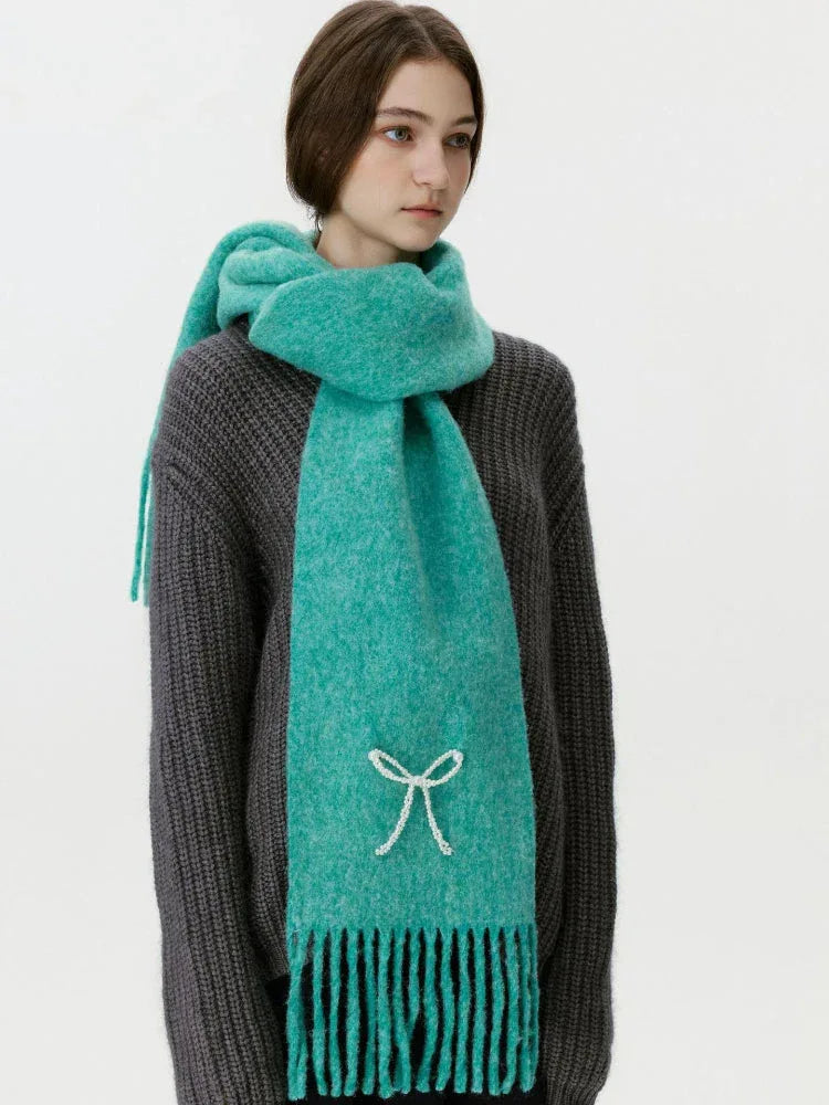 Woman wearing a teal scarf with a white bow embellishment and fringe.
