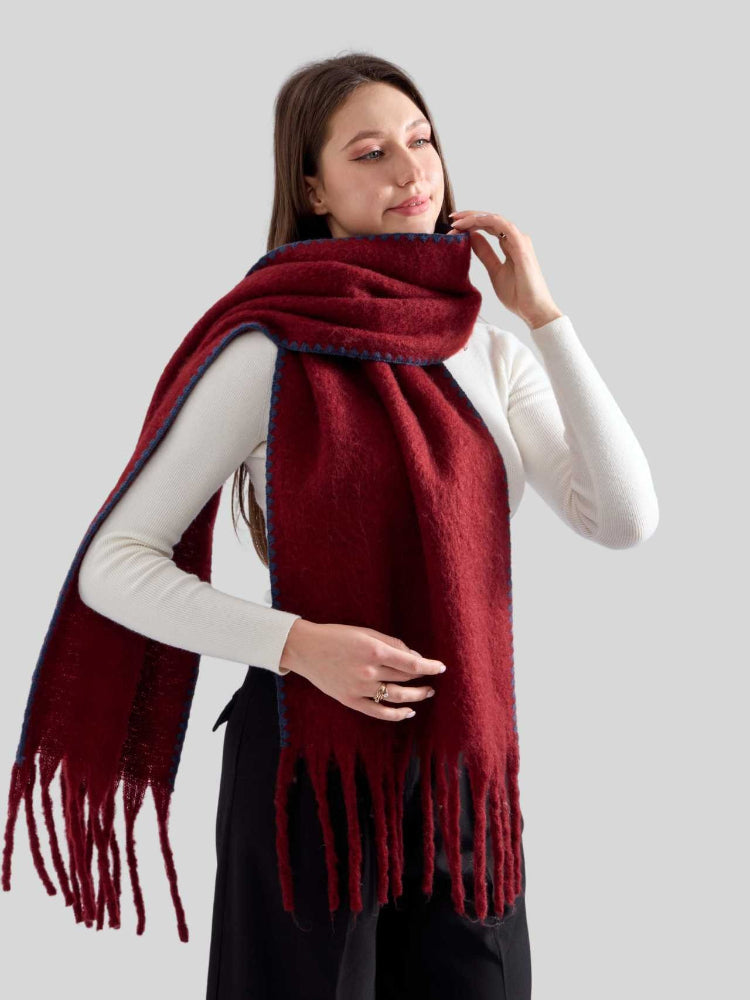 Woman wearing a burgundy knit scarf with fringed ends and blue contrast stitching.