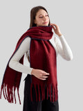 Close-up of a woman adjusting a burgundy knit scarf with fringed ends and blue contrast stitching.
