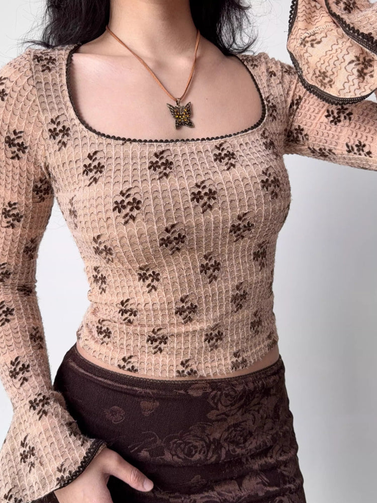 Close-up of a woman wearing a beige long-sleeved top with a brown floral print and a square neckline.