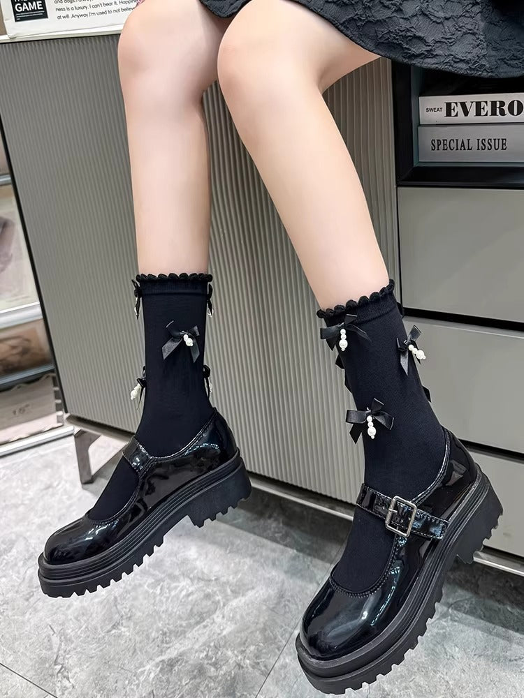 Black ankle socks with ruffled trim and black bow accents with pearl embellishments, paired with black platform mary jane shoes