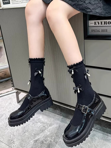 Black ankle socks with ruffled trim and black bow accents with pearl embellishments, paired with black platform mary jane shoes