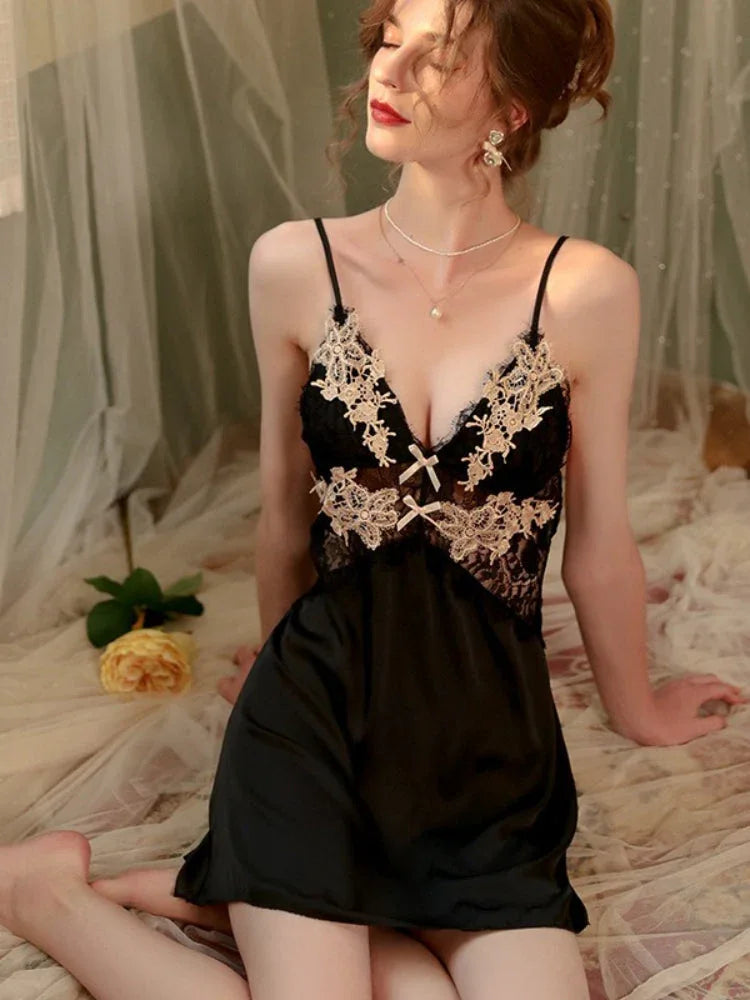 Woman wearing a black satin slip dress with lace detailing, seated on a bed with a yellow rose.