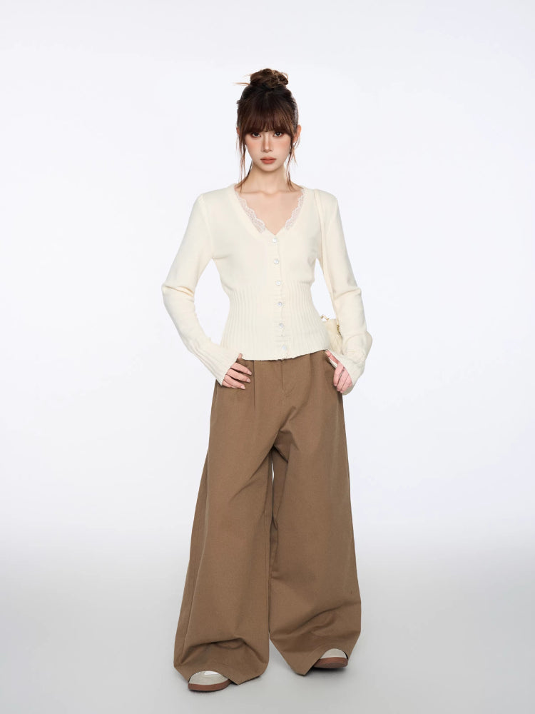 Full-body shot of a woman in a fitted cream cardigan and wide brown trousers.