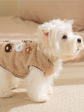 Rear view of a white dog wearing a tan fleece vest adorned with bear patches.