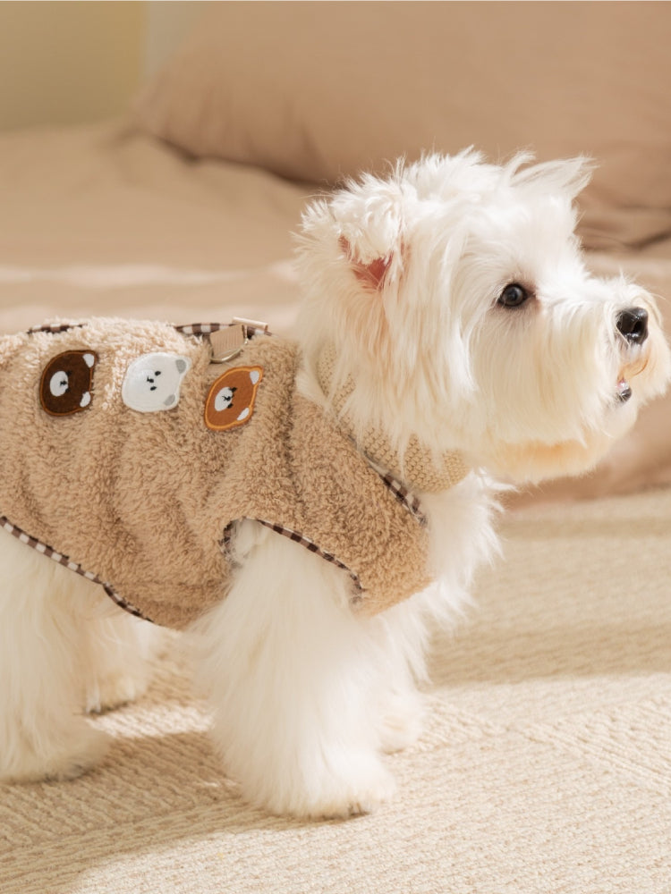 Rear view of a white dog wearing a tan fleece vest adorned with bear patches.