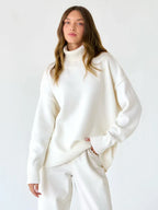 Woman wearing a white oversized turtleneck sweater and light wash wide-leg jeans.