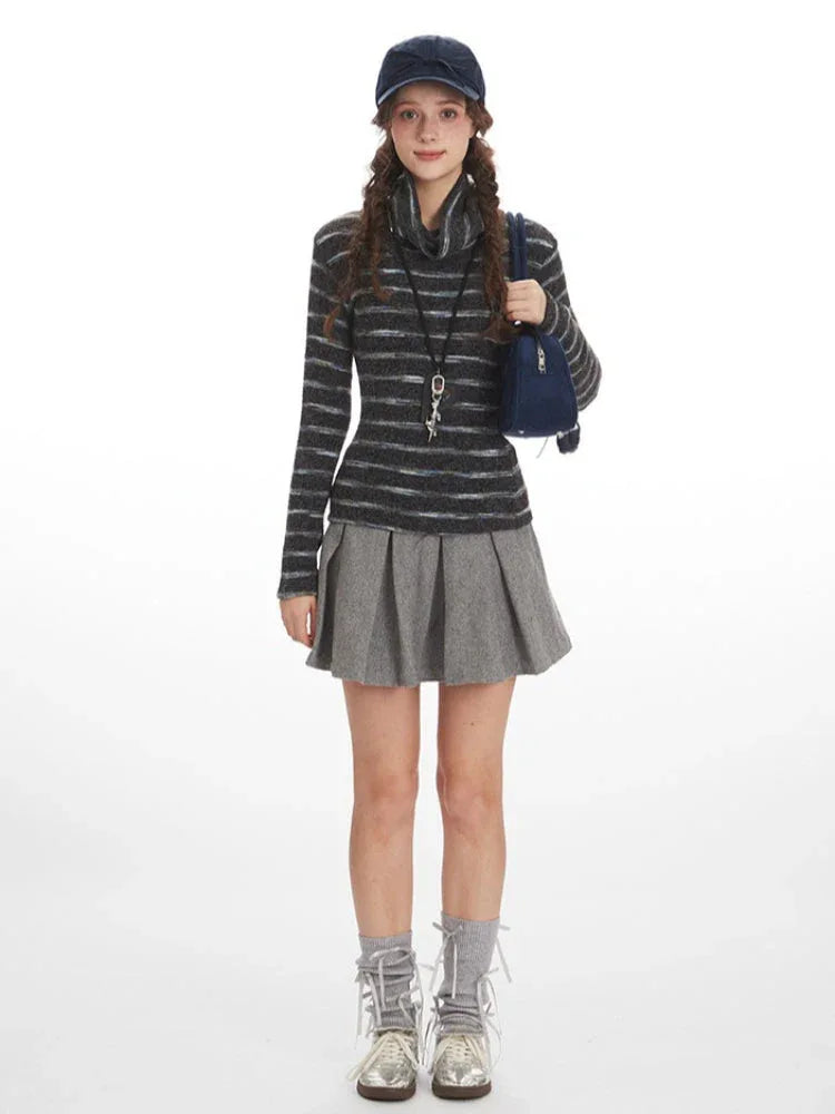 Model wearing a striped turtleneck sweater and a gray pleated mini skirt, with a navy blue baseball cap and a navy blue handbag.
