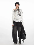 Woman wearing a white long-sleeve graphic print top with an off-the-shoulder design and black beanie.