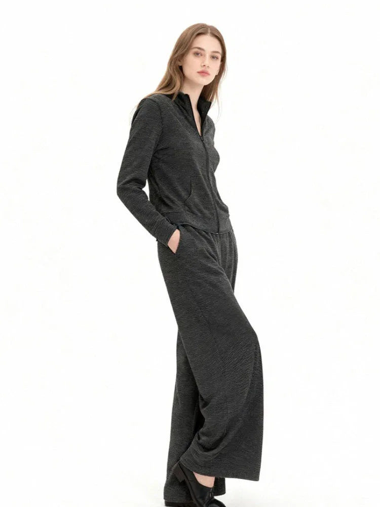 Woman wearing a charcoal grey knit loungewear set with a full zip jacket and wide leg pants, with hands in pockets.