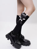 Detail of black knee-high socks with a whimsical cartoon cat applique, worn with black patent platform shoes.