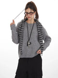Woman adjusting her scarf while wearing a grey crew neck sweater and black cargo pants