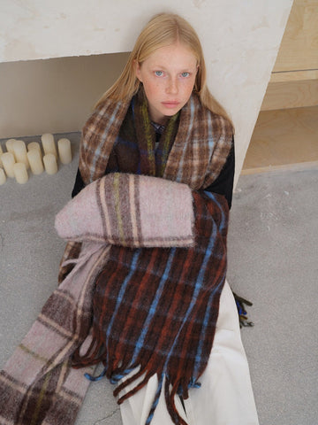 Woman wrapped in a plaid scarf with brown, blue, and pink tones