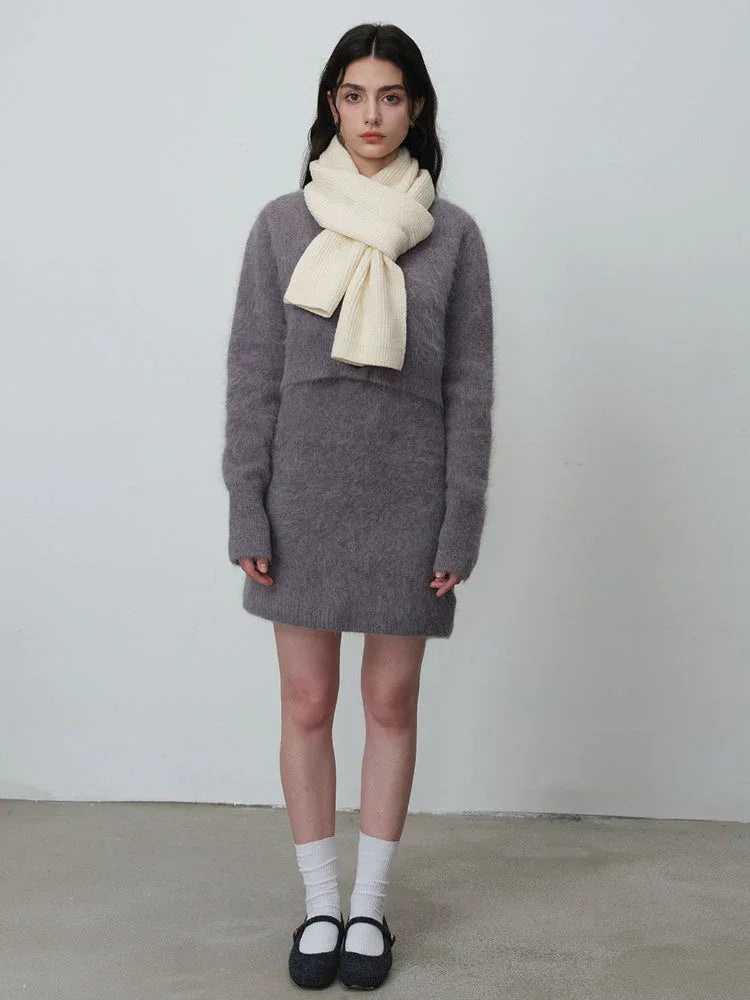 Full body shot of a woman wearing a cream-colored ribbed knit scarf, a grey fuzzy sweater dress, white socks, and black shoes