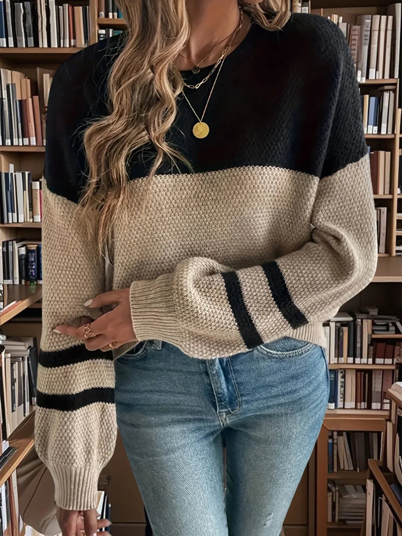 Woman wearing a black and beige color block knit sweater with striped cuffs and blue jeans. Main image
