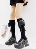 Black knee-high socks with a detachable plush toy embellishment on each leg, worn with black chunky sole sneakers.