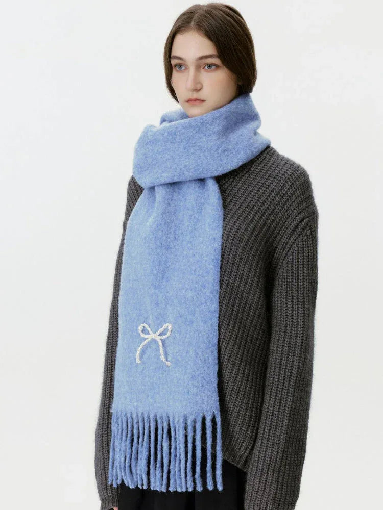 Woman wearing a light blue scarf with a white bow embellishment and fringe. Main image