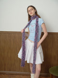 Woman in a light blue graphic t-shirt and white pleated skirt, posing with a colorful faux fur scarf.