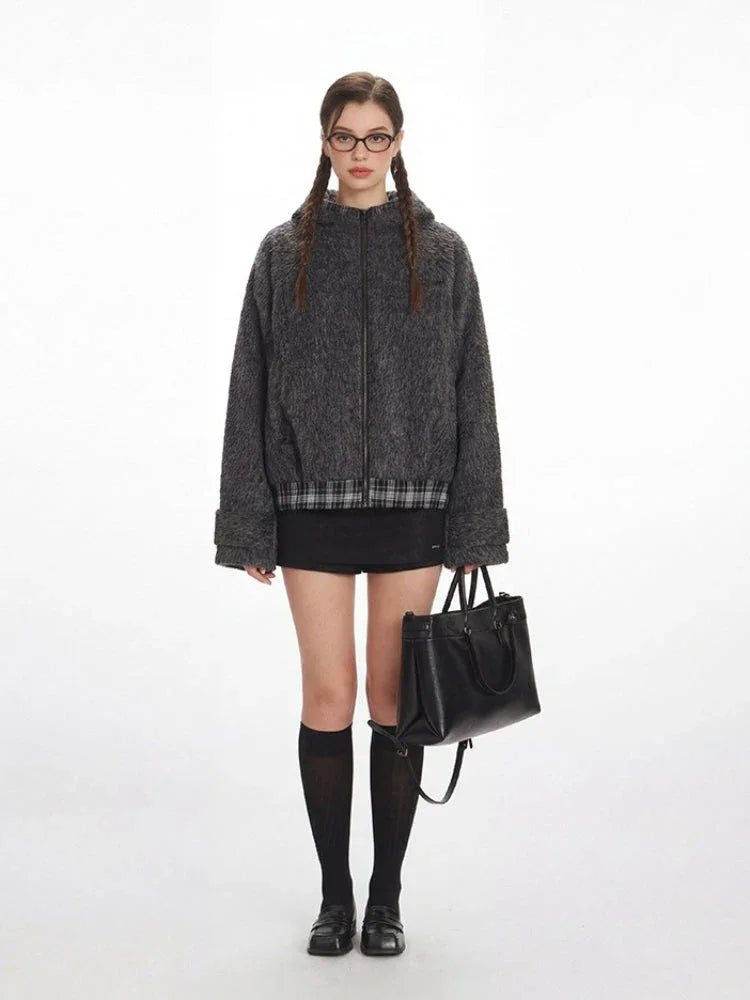 Woman wearing a grey fuzzy bomber jacket with plaid hem detail
