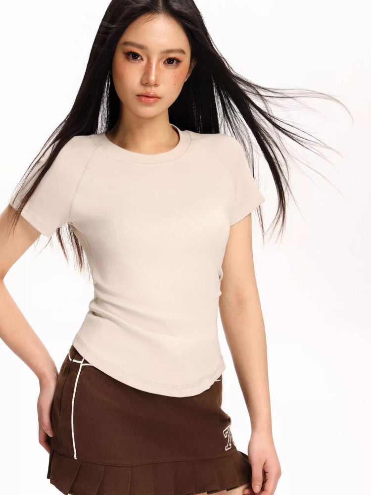 Woman wearing a beige fitted short-sleeve t-shirt and a brown pleated skirt
