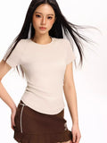 Woman wearing a beige fitted short-sleeve t-shirt and a brown pleated skirt