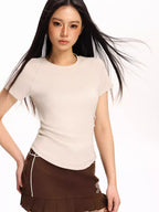 Woman wearing a beige fitted short-sleeve t-shirt and a brown pleated skirt