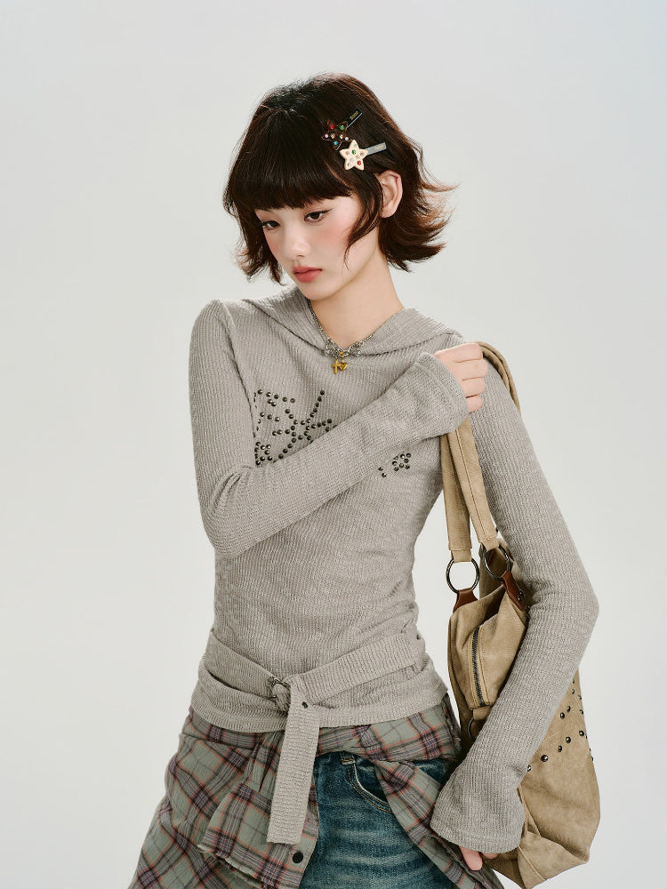 Model wearing a grey ribbed knit hooded long sleeve top with embellishments on the chest and a belted waist.