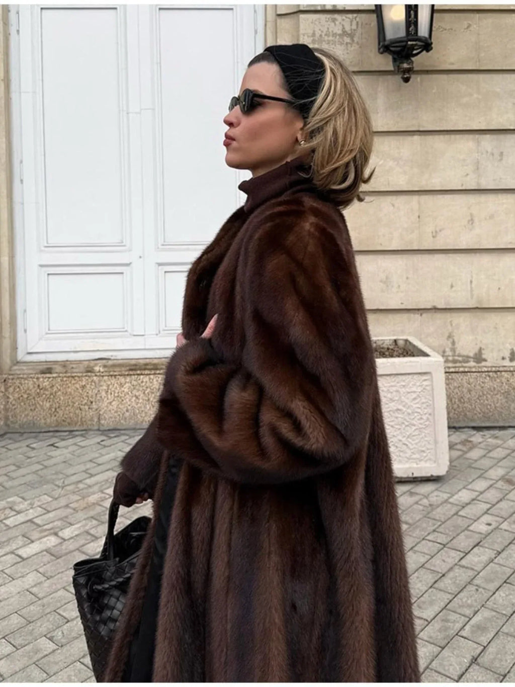 Side profile of a woman wearing a long brown mink fur coat, sunglasses, and a black headband.