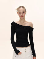 Woman wearing a black long-sleeved ruffled off-the-shoulder top and white wide-leg pants.