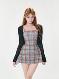 Full body shot of a woman in a black sheer bell sleeve cardigan and a red and blue plaid spaghetti strap mini dress.