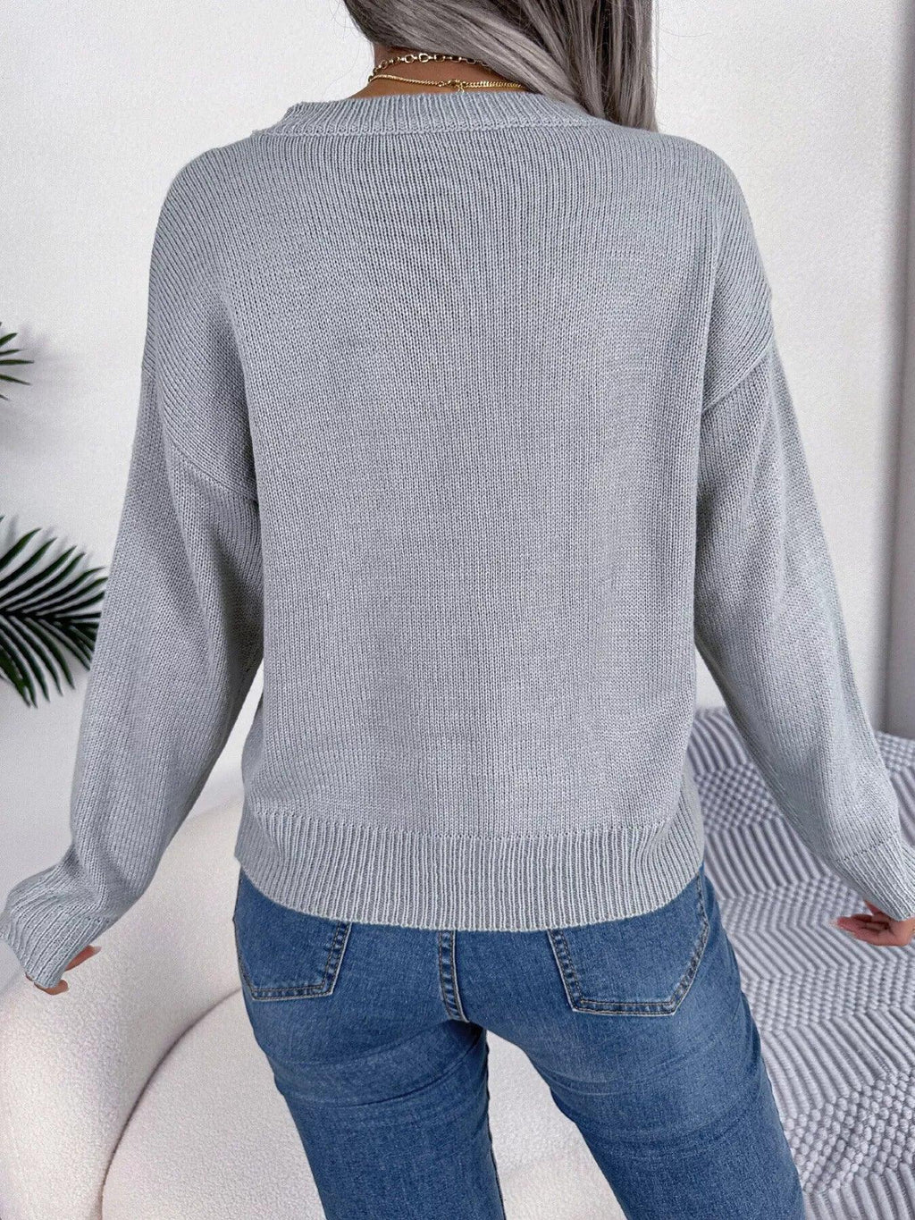 Back view of a woman wearing a grey long-sleeve knit sweater.