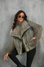 Woman in a grey faux fur jacket with hands in pockets, leaning.