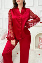 Woman wearing a red satin pajama set with sheer heart-patterned sleeves and ruffled details