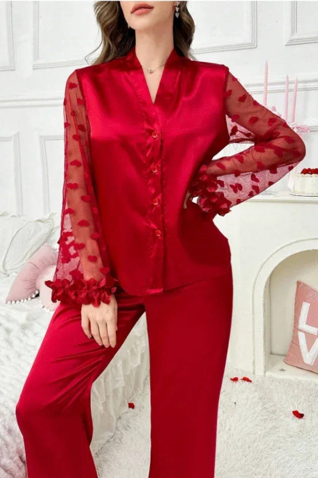 Woman wearing a red satin pajama set with sheer heart-patterned sleeves and ruffled details