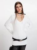 Woman posing in a white long-sleeve V-neck top, black belt, and dark wash jeans.