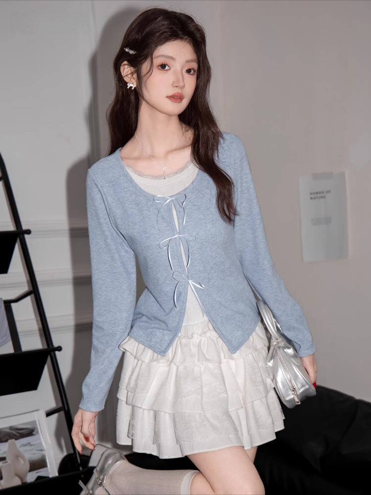 Woman wearing a light blue knit cardigan with white bow tie closures over a white top and a white tiered skirt.