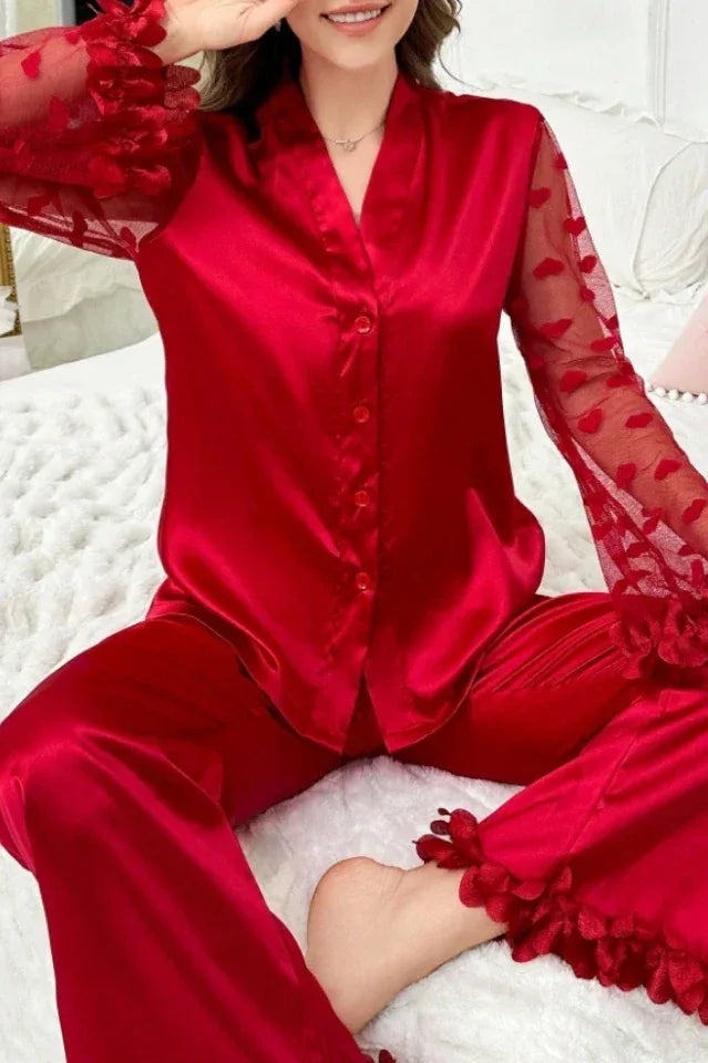 Woman sitting on a bed wearing a red satin pajama set with sheer heart-patterned sleeves