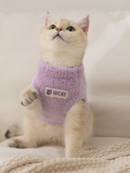 A light purple fluffy knit pet vest with a mock neck and a white logo patch on the front, worn by a light-colored cat.