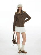 Woman wearing a brown cable knit cardigan with a faux fur collar and wooden buttons.