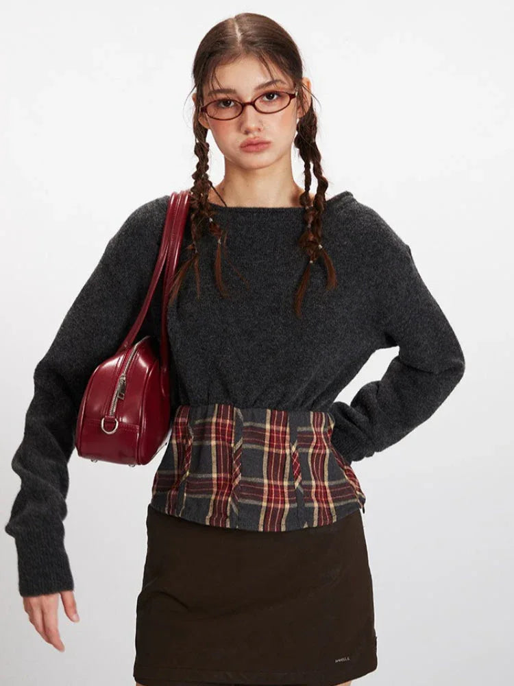Front view of a model carrying a red handbag, wearing a dark grey knit cropped sweater with a plaid waistband accent.
