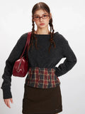 Front view of a model carrying a red handbag, wearing a dark grey knit cropped sweater with a plaid waistband accent.