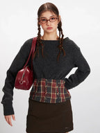 Front view of a model carrying a red handbag, wearing a dark grey knit cropped sweater with a plaid waistband accent.