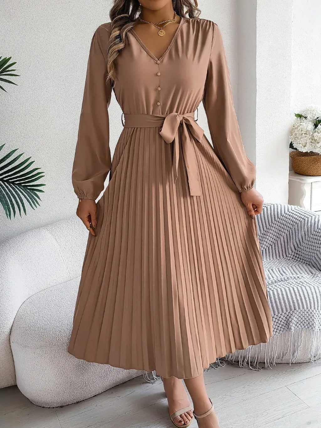 Woman wearing a brown long-sleeve V-neck midi dress with a pleated skirt and a self-tie belt