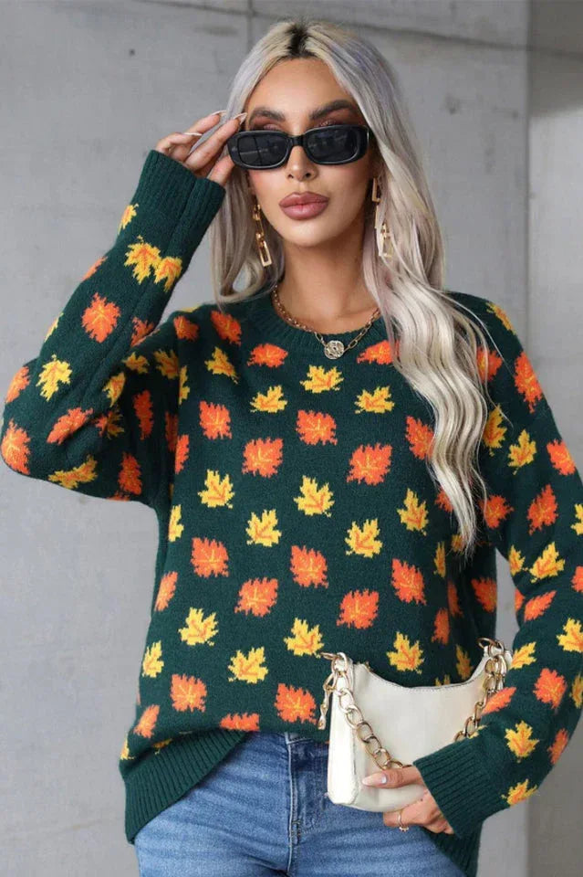 Woman wearing a dark green knit sweater with an all-over print of orange and yellow leaves.