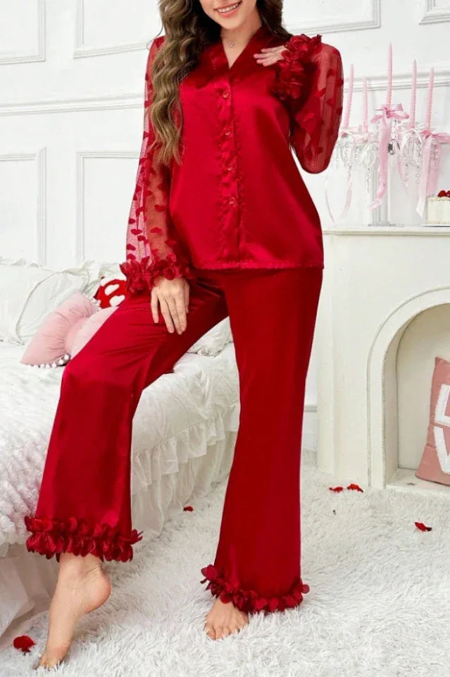Full body shot of a woman in a red satin pajama set with sheer heart-patterned sleeves and ruffled hems