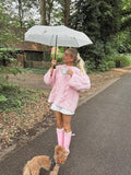 Woman walking outdoors in a pink oversized cable knit sweater and rain boots