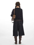 Back view of a woman in a navy long-sleeve top and dark wash denim culottes.