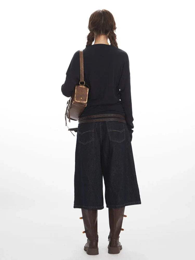 Back view of a woman in a navy long-sleeve top and dark wash denim culottes.
