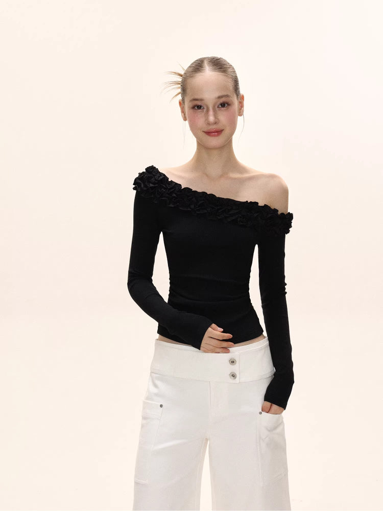Woman in a black long-sleeved ruffled off-the-shoulder top and white wide-leg pants, posing.