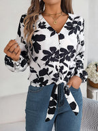Close-up of a woman wearing a white long-sleeve blouse with a black floral print and a tie-front detail.